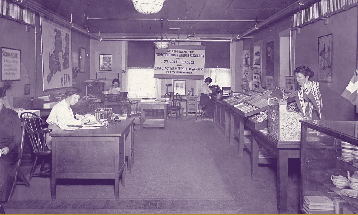 A shopfront office with suffrage posters in the windows.