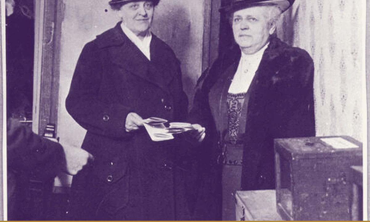 Two women at a polling place putting ballots into a box.