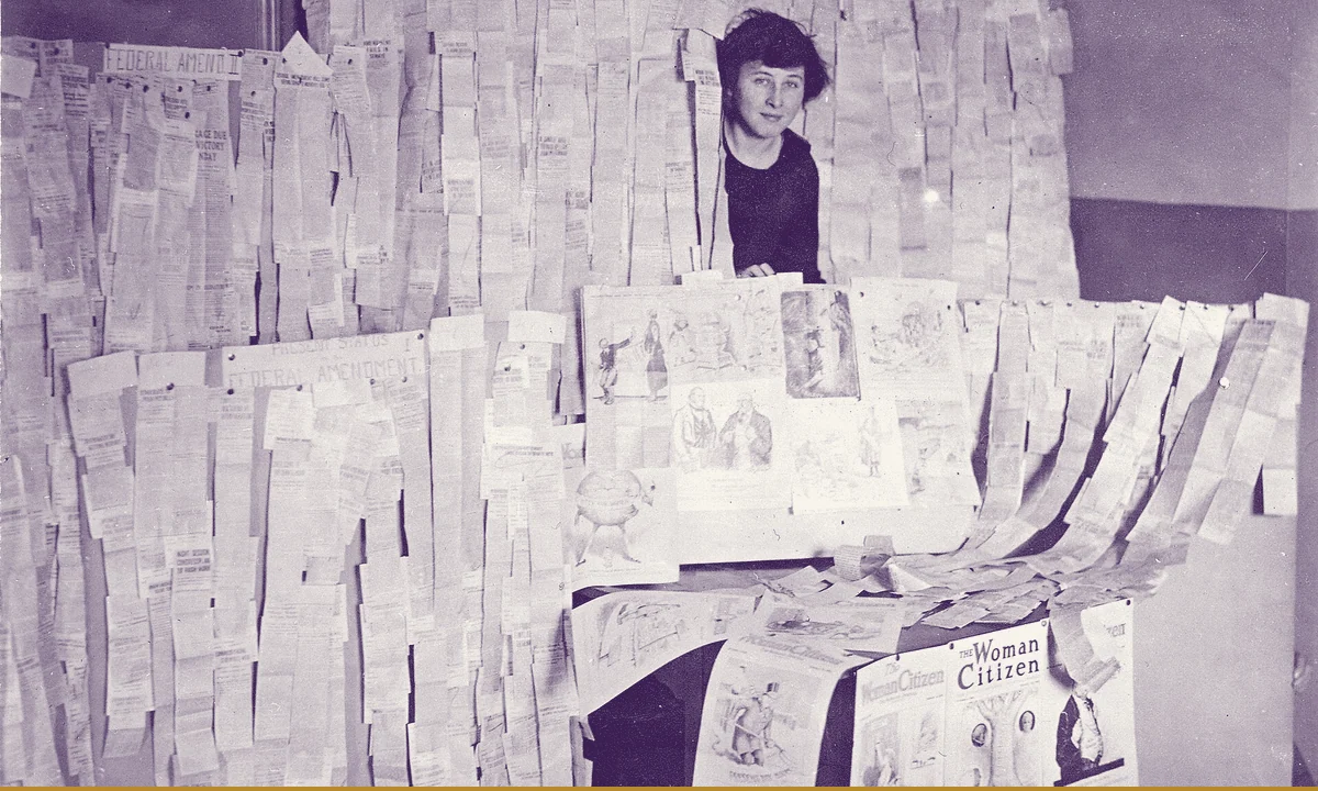 A woman holding up long strips of newspaper clippings reporting the Senate vote.